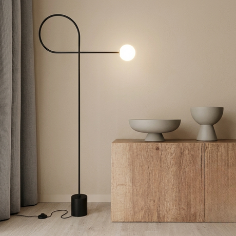 Skulpturale schwarze Stehleuchte mit minimalistischem Bogen und leuchtender Glaskugel in einem warmen, beige-farbenen Japandi-Interieur auf hellem Holzboden.