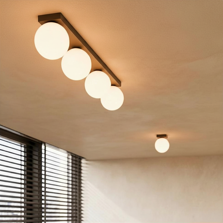Vierflammige Deckenleuchte mit opalen Glaskugeln auf schwarzer Metallschiene in einem warmen, beige-farbenen Interieur im minimalistischen Japandi-Stil.